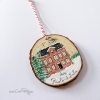 Décoration de Noël peinte sur rondin montrant une maison rouge et des sapins enneigés