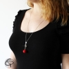 Long sautoir pomme d'amour rouge portée sur le décolleté d'un haut couleur noir 